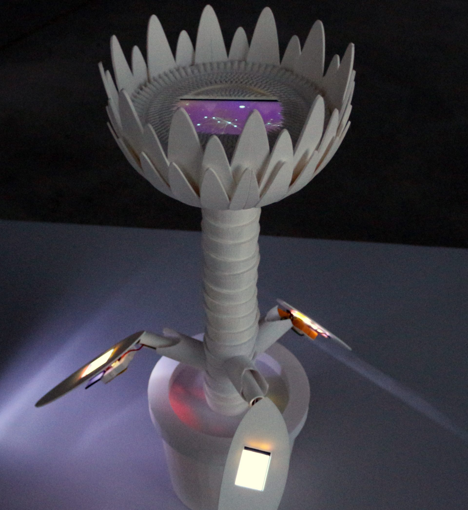 a white 3D printed flower like being with lcd screens and lights
