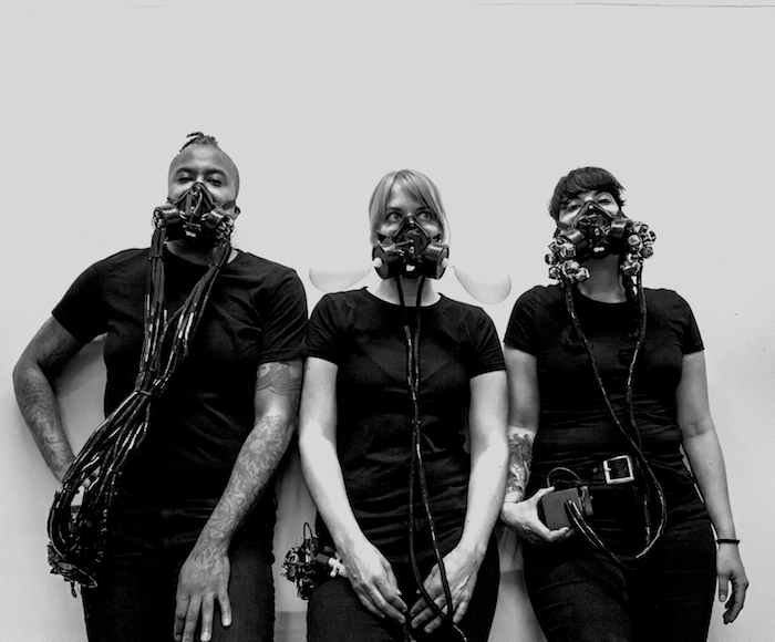 Three people wearing custom wearable instruments made of gas masks