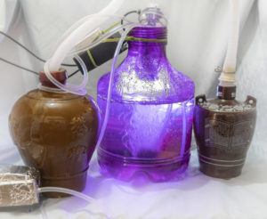 Three bottles of various makes and sizes with tubes and wires running around. The middle bottle has water, air bubbles, and light